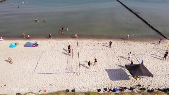 An einem Strand spielen mehrere Beachvolleyballerinnen auf einem Beachvolleyballfeld. © Screenshot 