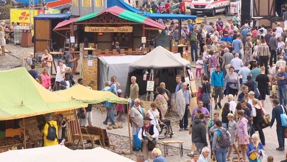 Blick aus der Ferne auf einen gut gefüllten Marktplatz auf dem sich viele Besucher zwischen bunten Ständen des Schwedenfests in Wismar tummeln. © Screenshot 
