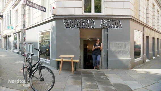 Eine Frau steht im Eingang eines Restaurants an einer Straßenecke im Hamburger Karoviertel, über ihr steht in Graffiti-Lettern: "Bodega Lima". © Screenshot 