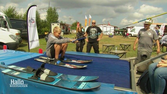 Ein junge trainiert auf einer beweglichen Plastikunterlage Wasserski zu fahren. © Screenshot 