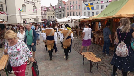 Schauspieler gehen in historischerschwedischer Kleidung zwischen den Ständen des Schwedenfests in Wismar über den Marktplatz. © Screenshot 