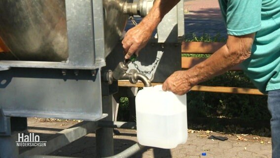 Ein Mann füllt sich Trinkwasser von einem Tank in einen Kanister ab. © Screenshot 
