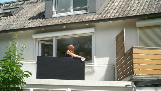 Eine Frau putzt ein Solarpanel, das am Geländer ihres Balkons angebracht ist. © Screenshot 