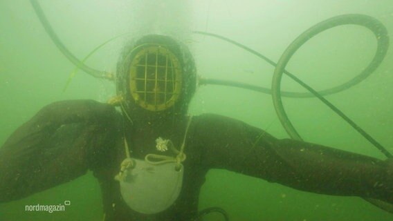 Ein Taucher mit historischem Tauchanzug im grünlich schimmernden Wasser. © Screenshot 