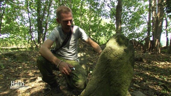 Hendrik Altmann kniet neben einem alten Grabstein © Screenshot 