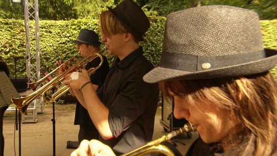 Drei junge Männer mit Hüten spielen Trompete © Screenshot 