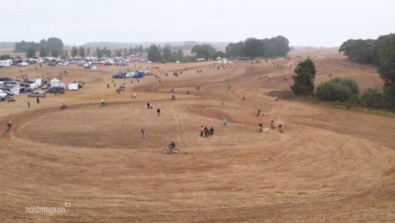 Blick aus der Vogelperspektive auf ein Stoppelfeld auf dem viele Motocross-Fahrende in Kreisen umherfahren. © Screenshot 