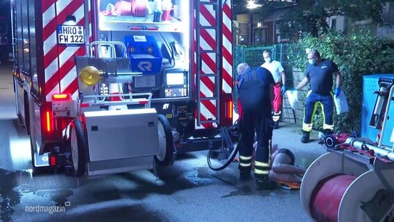 Einsatzkräfte der Feuerwehr duschen einen auf der Straße liegenden Mann bei Nacht mit einem Wasserschlauch ab. © Screenshot 