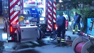 Einsatzkräfte der Feuerwehr duschen einen auf der Straße liegenden Mann bei Nacht mit einem Wasserschlauch ab. © Screenshot 