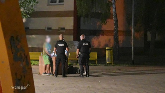 Blick aus der Ferne auf zwei Streifenpolizisten, die bei Nacht in einem Wohngebiet mit zwei unkenntlich gemacht Personen sprechen. © Screenshot 