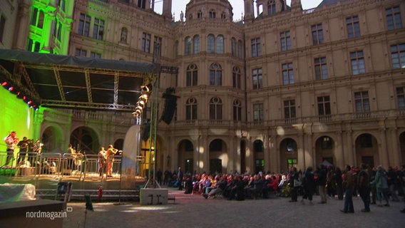 Bei einem Auftritt einer Blasband im Innenhof des Schweriner Schlosses schauen mehrere Menschen zu. © Screenshot 