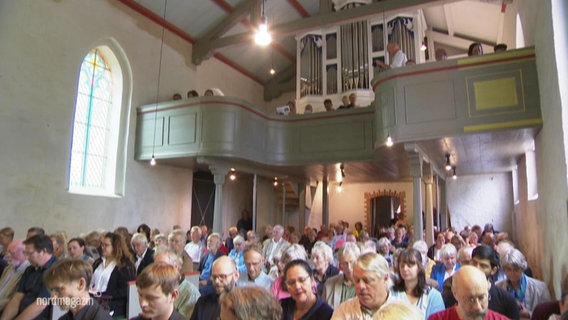 Blick in ein Kirchenschiff vom Altar aus in dem eine vollbesetzte Gemeinde bei einem Gottesdienst sitzt, im Hintergrund: eine Orgel. © Screenshot 