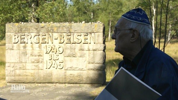 Neben der Gedenktafel vom KZ Bergen-Belsen steht der Überlebende Alfred Garwood. © Screenshot 