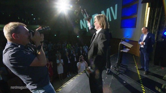 Matthias Habich hält den "Goldenen Ochsen" auf der Bühne empor und zeigt ihm dem Publikum. Neben ihm macht ein Fotograf Bilder von ihm. © Screenshot 