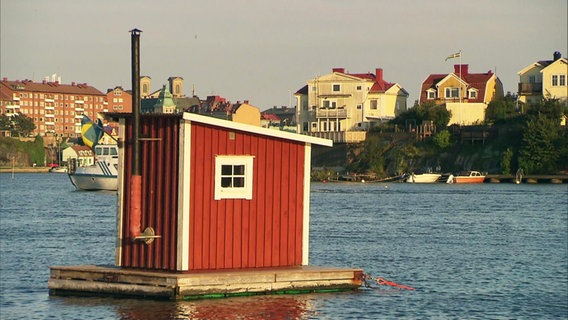 Ein schwedisches Fischerhäuschen steht im Hafen vor einer Stadt © Screenshot 