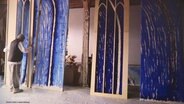 Der Künstler Günther Uecker steht vor seinen Entwürfen blauer Kirchenfenster. © Screenshot 