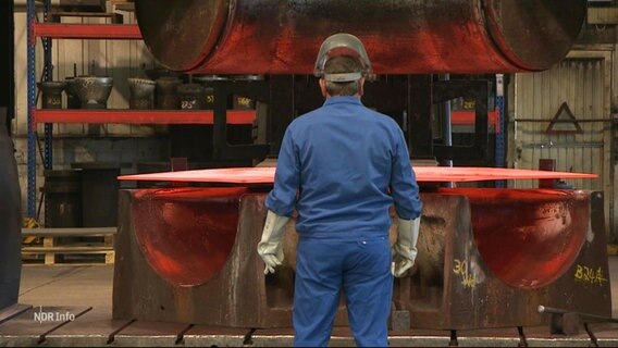 Ein Arbeiter in einem Blaumann steht vor einem größeren Rohr, das in einer Fabrik geformt wird. © Screenshot 