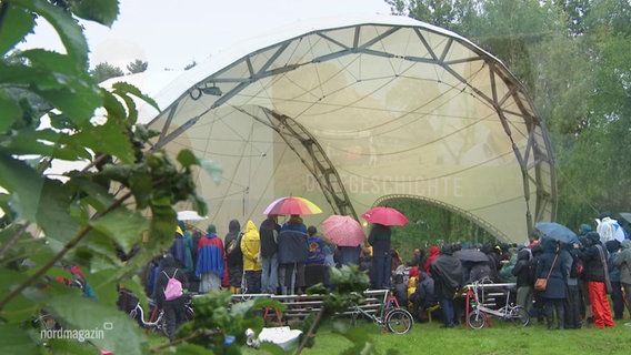 Menschen kommen im Regen unter einem Theaterzelt zusammen. © Screenshot 