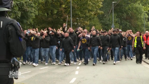 Ein Block von Fans eines Fußballvereins läuft schwarz gekleidet auf einer Straße. © Screenshot 