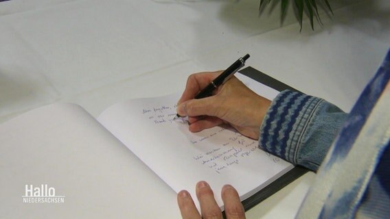 Eine Hand schreibt mit einem Stift in ein Kondolenzbuch. © Screenshot 