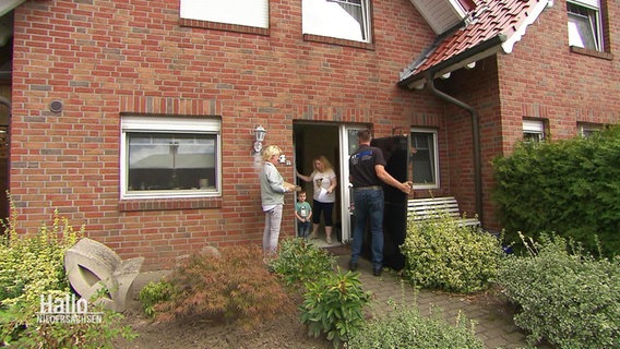 An der Haustür eines Wohnhauses stehen die Bewohner sowie ein Mann, der eine Photovoltaikanlage anliefert. © Screenshot 