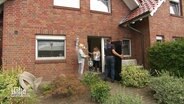 An der Haustür eines Wohnhauses stehen die Bewohner sowie ein Mann, der eine Photovoltaikanlage anliefert. © Screenshot 