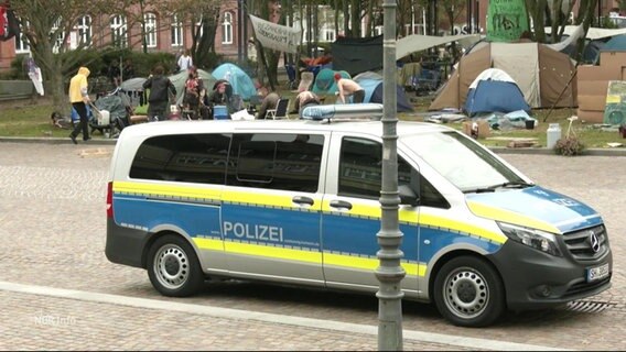 Ein Polizieauto parkt auf einer Straße, im Hintergrund mehrere Zelte. © Screenshot 