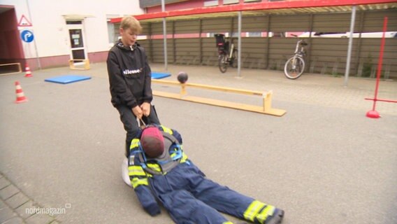 Ein Junge bekommt einen Crashkurs bei der Feuerwehr. © Screenshot 