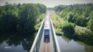 Ein blauer Zug fährt über eine Brücke. © Screenshot 