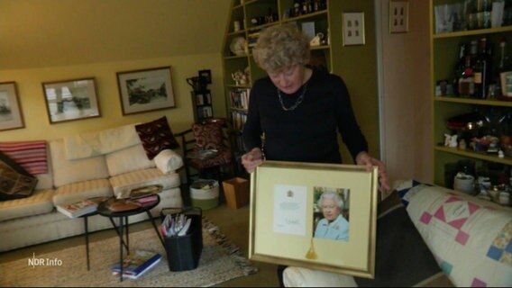 Eine Frau hält einen eingerahmten Brief der Queen hoch. © Screenshot 