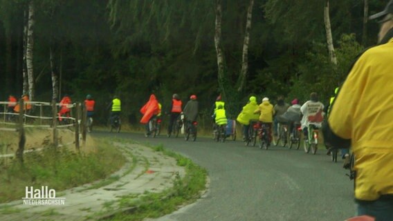 Eine Kette von Radfahrenden fährt um eine Kurve auf einer Landstraße bei Regen. © Screenshot 