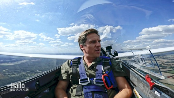 Moderator Arne-Torben Voigts sitzt im Cockpit eines Segelflugzeugs und genießt die Aussicht. © Screenshot 