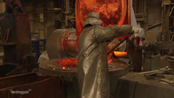Eine Person in silberner Hitze-Schutzkleidung rührt in einem Schmelztiegel in einem Metallgusswerk. © Screenshot 