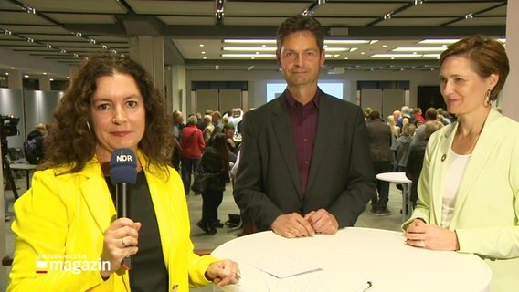 Reporterin Simone Mischke (li.) schaut in die Kamera. Neben ihr stehen Fabian Geyer (mitte., parteilos) und Amtsinhaberin Simone Lange (re., SPD). © Screenshot 