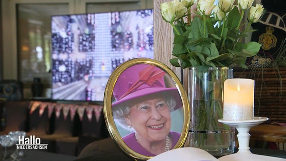 Ein Foto von Queen Elisabeth II., auf einem Fernseher im Hintergrund läuft eine Übertragung ihrer Trauerfeier. © Screenshot 