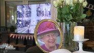 Ein Foto von Queen Elisabeth II., auf einem Fernseher im Hintergrund läuft eine Übertragung ihrer Trauerfeier. © Screenshot 