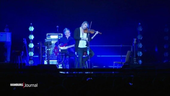 Geiger David Garret steht in blaues Scheinwerferlicht getaucht auf einer größeren Bühne spielt verträumt auf seiner Violine. © Screenshot 