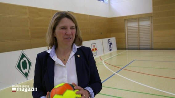 Die schleswig-holsteinische Justiz- und Gesundheitsministerin Kerstin von der Decken hält einen Fußball in der Hand und steht in einer Sporthalle. © Screenshot 