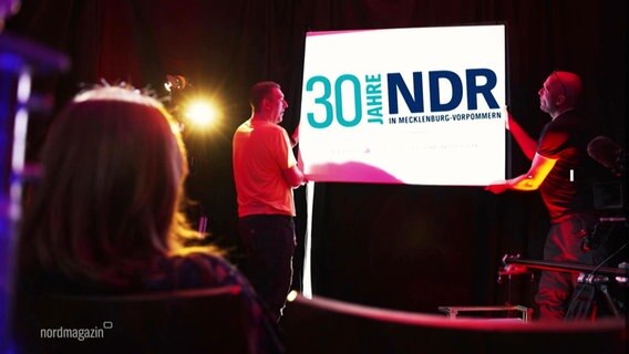 Auf einer Bühne wird ein Schild, das 30 Jahre NDR in MV feiert, getragen © Screenshot 