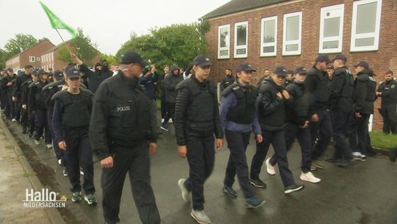 Mehrere Praktikanten bei der Bundespolizei begleiten gespielte Fußballfans in Blockformation auf einem Trainingsgelände. © Screenshot 