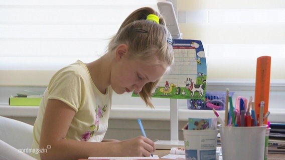 Ein jüngeres Mädchen sitzt konzentriert gebeugt über Schulaufgaben an einem Schreibtisch. © Screenshot 