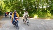 Moderator Yared Dibaba fährt mit weiterern Mitstreitern einen begrünten Wanderweg auf dem Fahrrad entlang. © Screenshot 