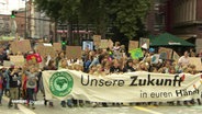 Ein Demozug bewegt sich auf einer großen, mehrspurigen straße. Die Vordersten halten ein größeres Banner von Fridays For Future. © Screenshot 