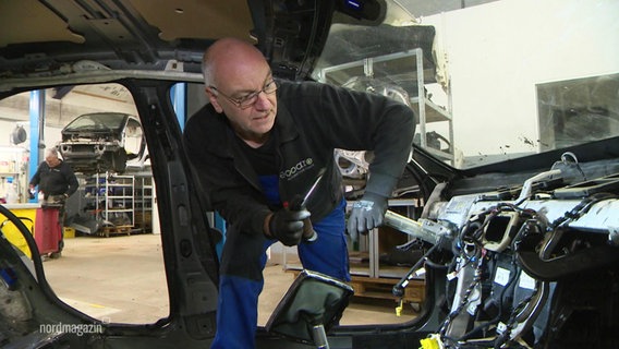 Mechatroniker Rold Knauer von der Firma ecCARo schaut in einem Autowrack, welche Teile er noch verwerten kann. © Screenshot 