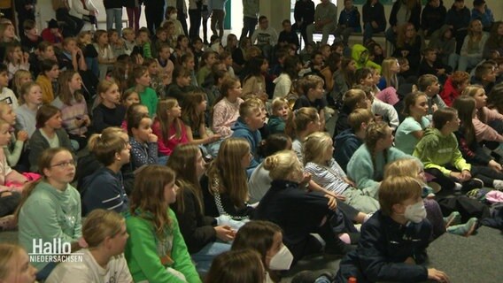 Viele Schülerinnen sitzen erwartungsvoll in einer Aula. © Screenshot 