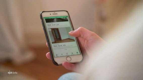 Eine Person sucht auf einem Mobiltelefon nach Wohnungen, auf dem Display ist eine Zimmertür zu sehen. © Screenshot 