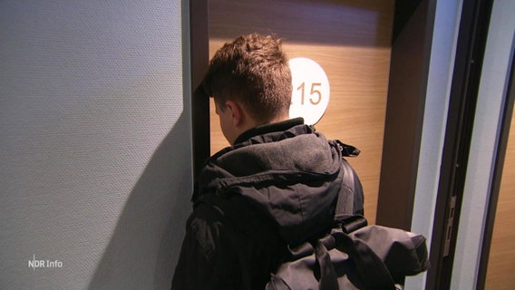 Ein junger Mann steht vor einer Tür mit der Nummer 15. © Screenshot 