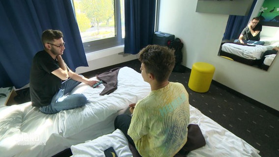Zwei junge Männer sitzen in einem Hotelzimmer. © Screenshot 