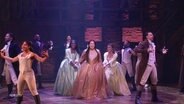 In einer Musicalszene aus "Hamilton" tanzen und singen mehrere Menschen auf einer Bühne. © Screenshot 