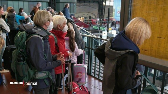 Bahnreisende warten im Hamburger Bahnhof. Viele haben ihre Koffer mit dabei. Einigetragen eine Mund-Nasen-Bedeckung. © Screenshot 